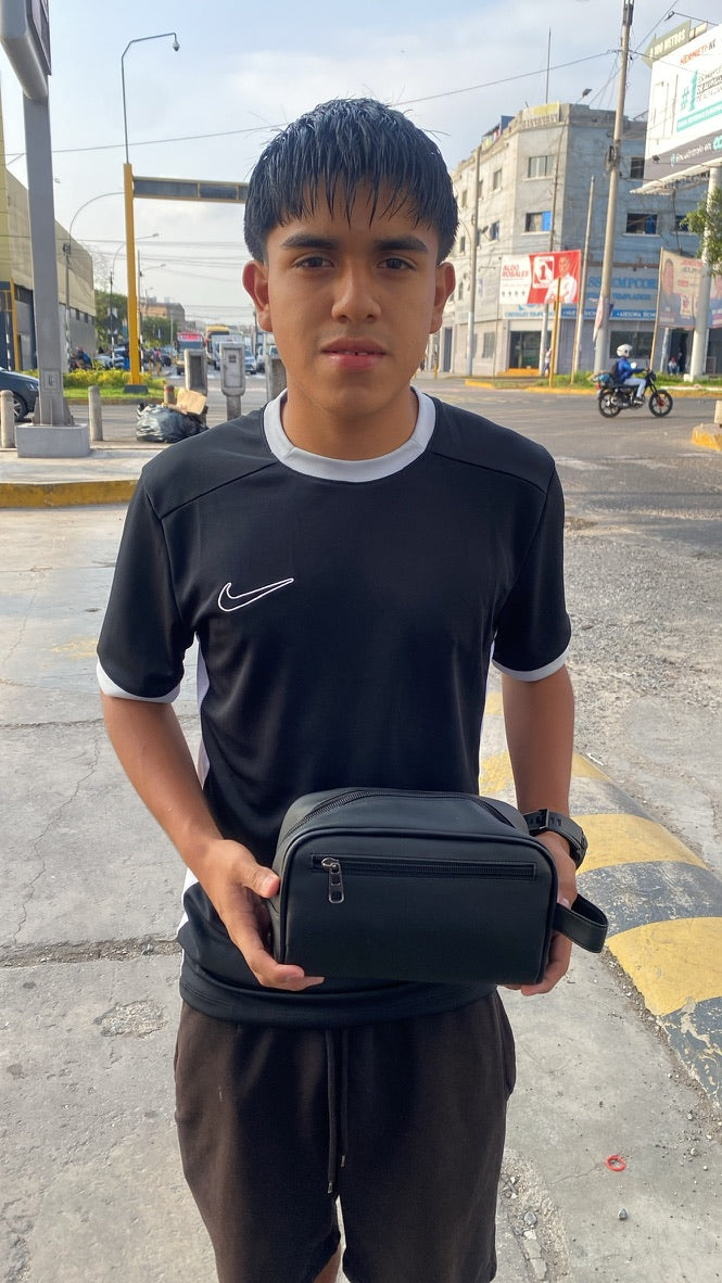 Una persona mostrando un neceser negro en exterior.